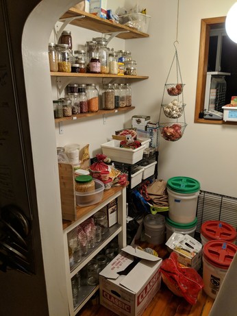 A series of wall shelves and carts filled with food in a pantry.