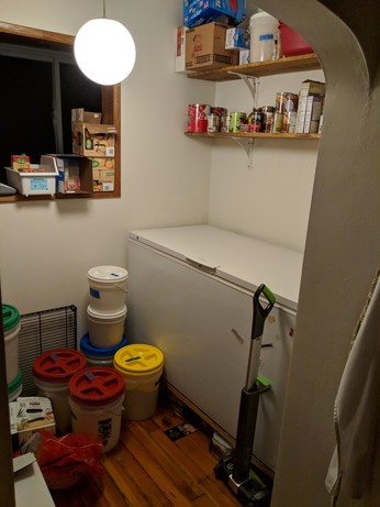 A large deep freeze and more pantry shelves. There are large buckets on floor. 