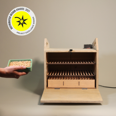 picture of our incubator, with a sticker that says "project excellence winner", and a hand bringing a tempeh mold to the incubator